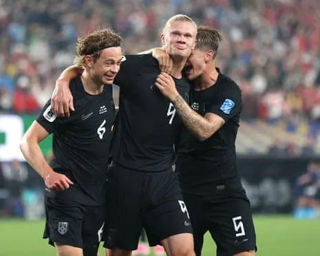 Three Norway players including Erling Haaland celebrate together on a pitch, arms around each other
